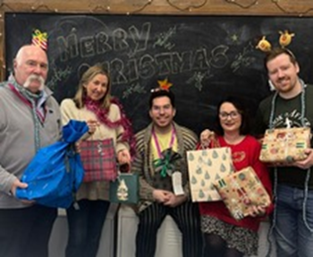 Group of people dressed in festive clothing holding wrapped gifts