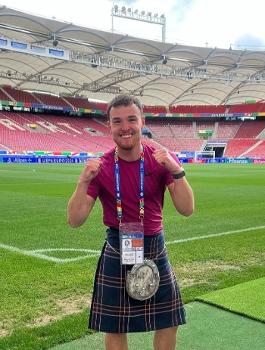 Man wearing a kilt stand in front of pitch in an empty football stadium