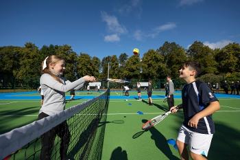 A girl bats a tennis ball over the net to a boy who stands posed to bat it back to her