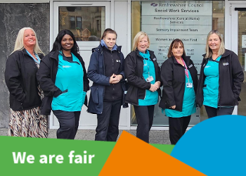 Group of women in blue/green carer uniforms stand smiling to camera