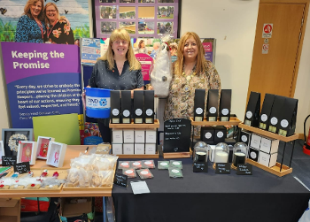 Two women stand behind a table with a range of small gifts for sale