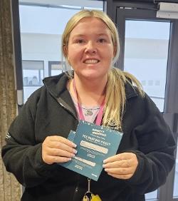 A smiling woman holds two blue tickets to ice-skating