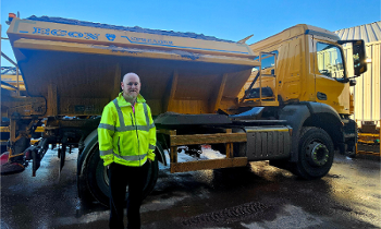 A man in a high-vis jacket stands in front of a gritting vehicle