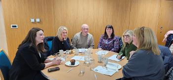 Minister for Children, Young People and The Promise, Natalie Don-Innes, sits at a round table and talks to four women and one man, who are foster carers, at an event for foster carers.